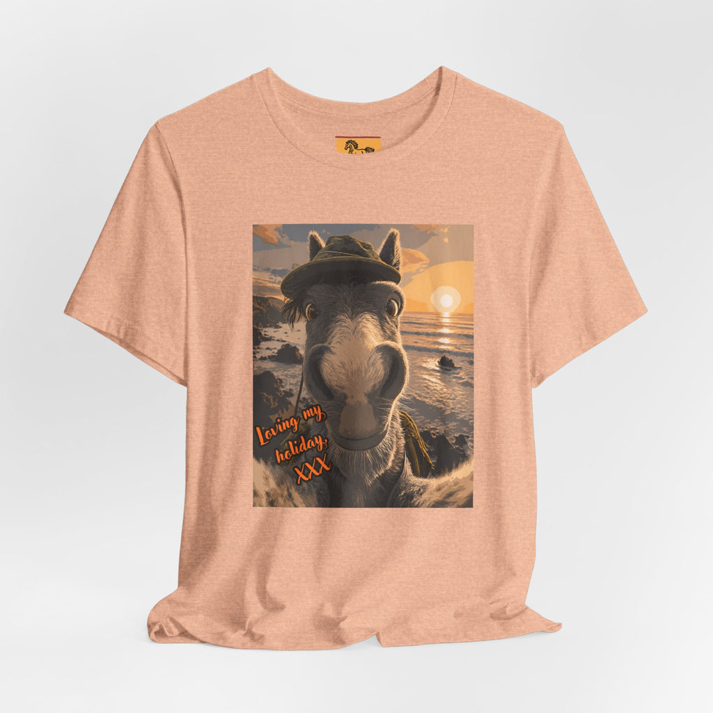A Bella + Canvas 3001 unisex t-shirt featuring an illustrated horse taking a beach selfie at sunset, wearing a hat, with the words 'Loving my holiday XXX' in orange script. 