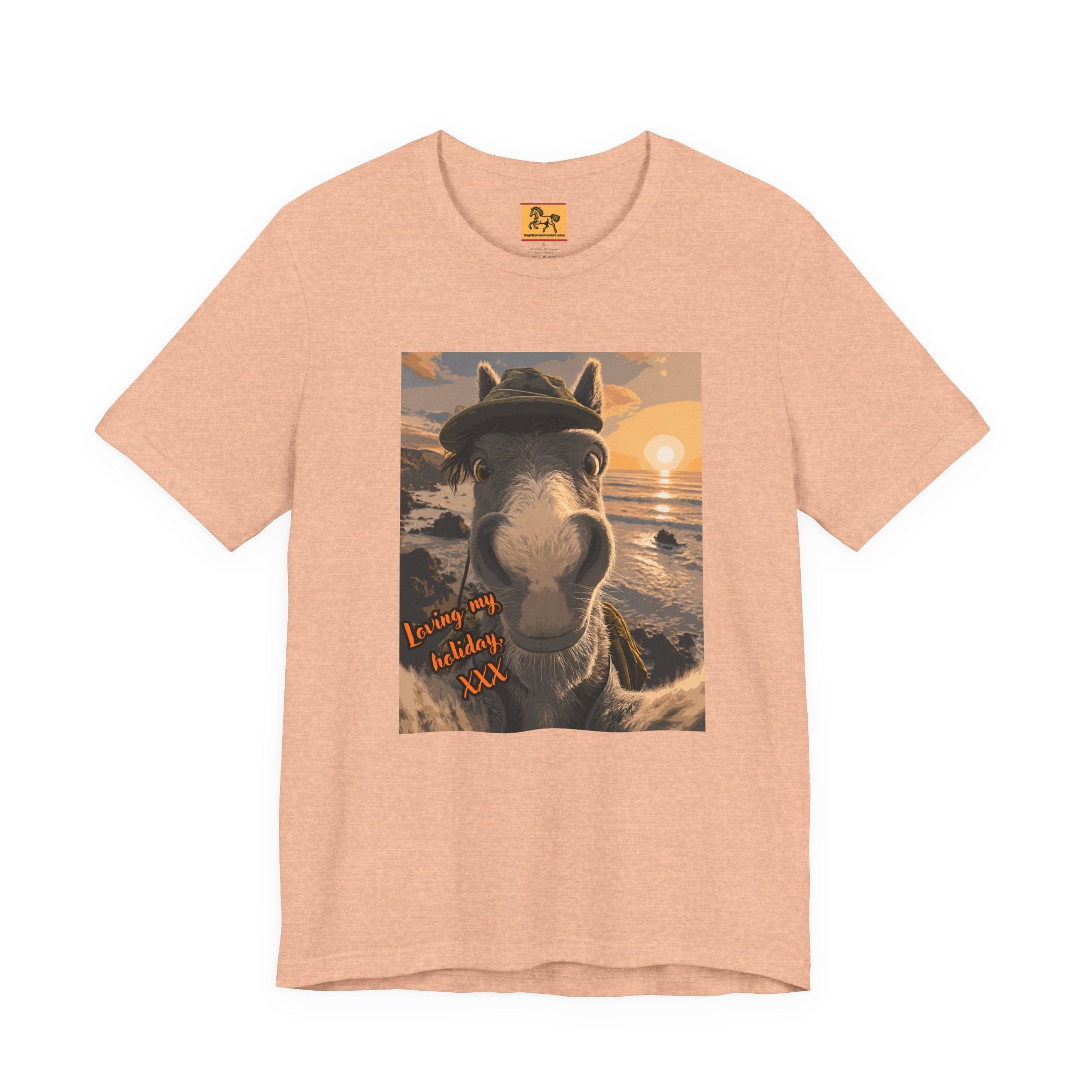 A peach Bella + Canvas 3001 unisex t-shirt featuring an illustrated horse taking a beach selfie at sunset, wearing a hat, with the words 'Loving my holiday XXX' in orange script. 
