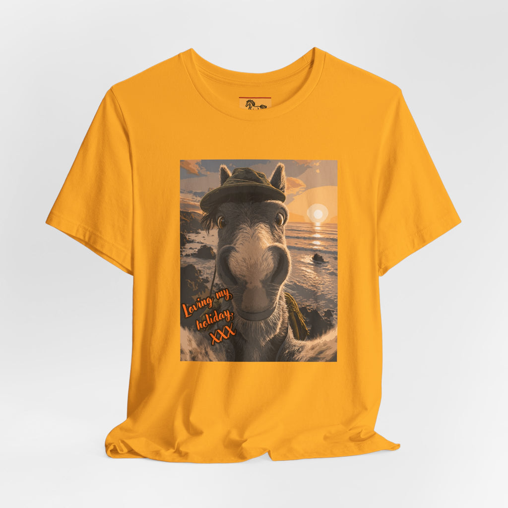 A Bella + Canvas 3001 unisex t-shirt featuring an illustrated horse taking a beach selfie at sunset, wearing a hat, with the words 'Loving my holiday XXX' in orange script. 