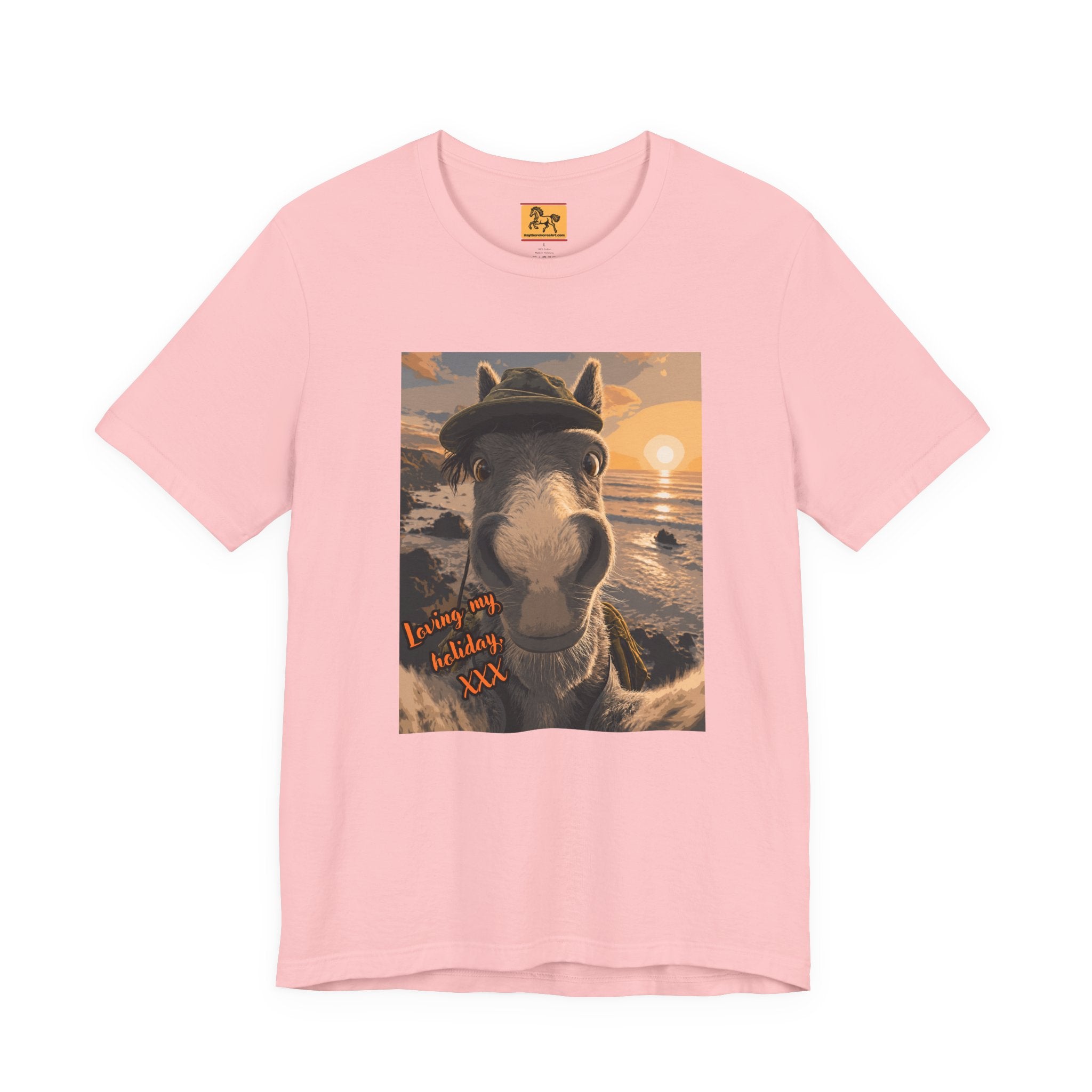 A light pink Bella + Canvas 3001 unisex t-shirt featuring an illustrated horse taking a beach selfie at sunset, wearing a hat, with the words 'Loving my holiday XXX' in orange script. 