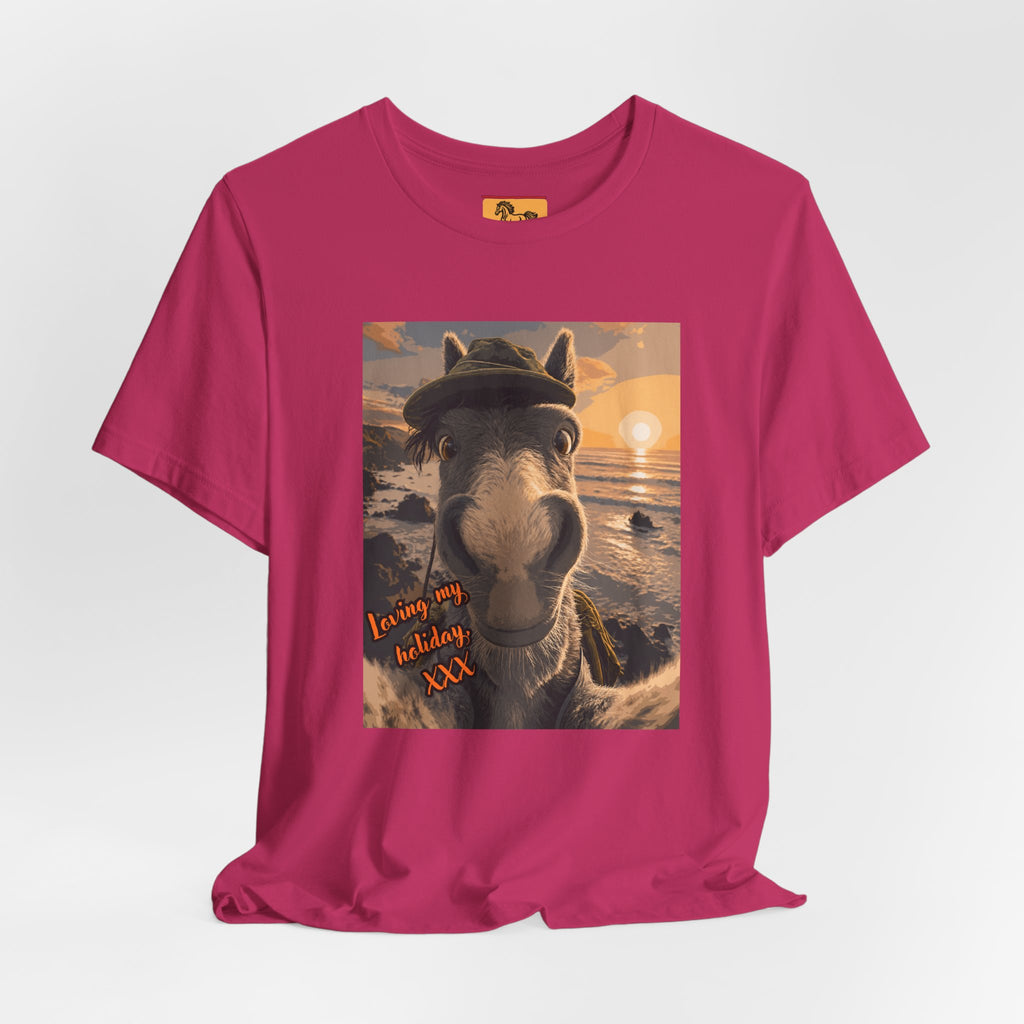 A Bella + Canvas 3001 unisex t-shirt featuring an illustrated horse taking a beach selfie at sunset, wearing a hat, with the words 'Loving my holiday XXX' in orange script. 
