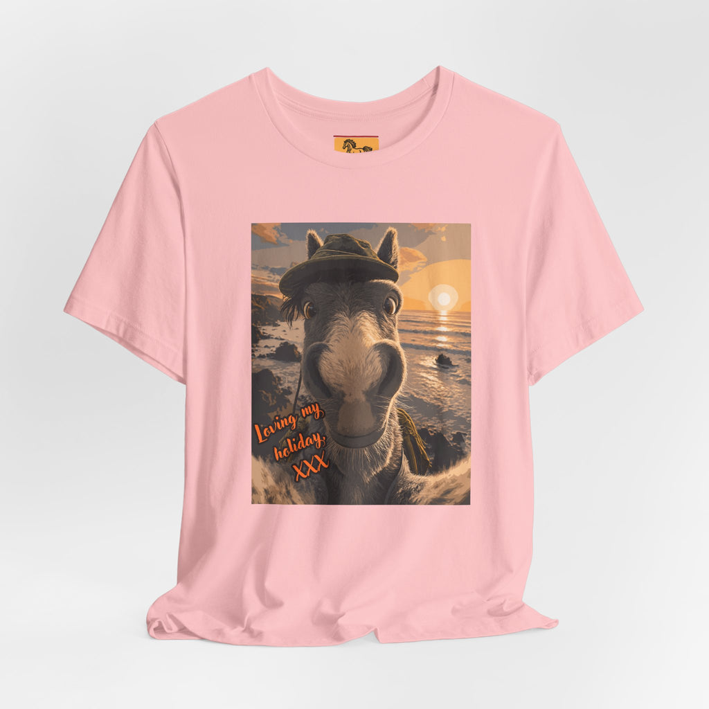 A Bella + Canvas 3001 unisex t-shirt featuring an illustrated horse taking a beach selfie at sunset, wearing a hat, with the words 'Loving my holiday XXX' in orange script. 