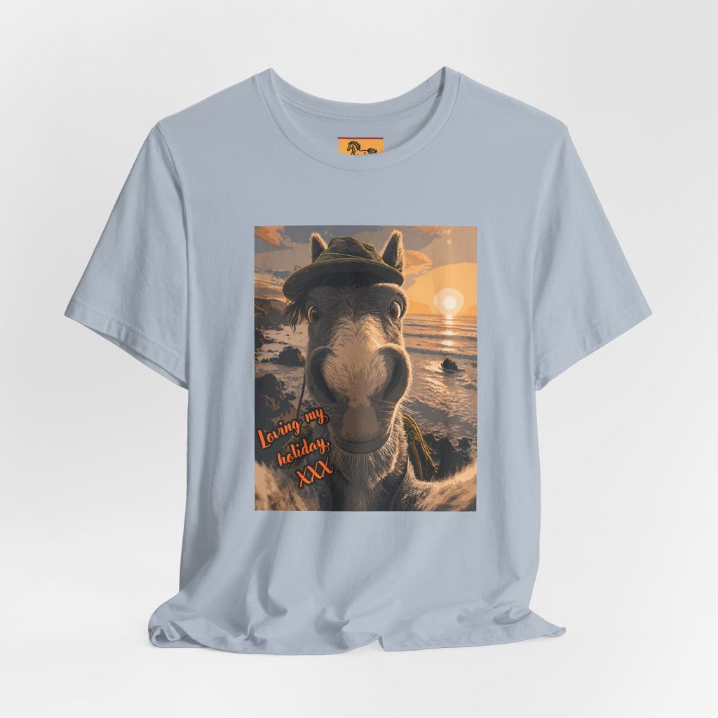 A Bella + Canvas 3001 unisex t-shirt featuring an illustrated horse taking a beach selfie at sunset, wearing a hat, with the words 'Loving my holiday XXX' in orange script. 