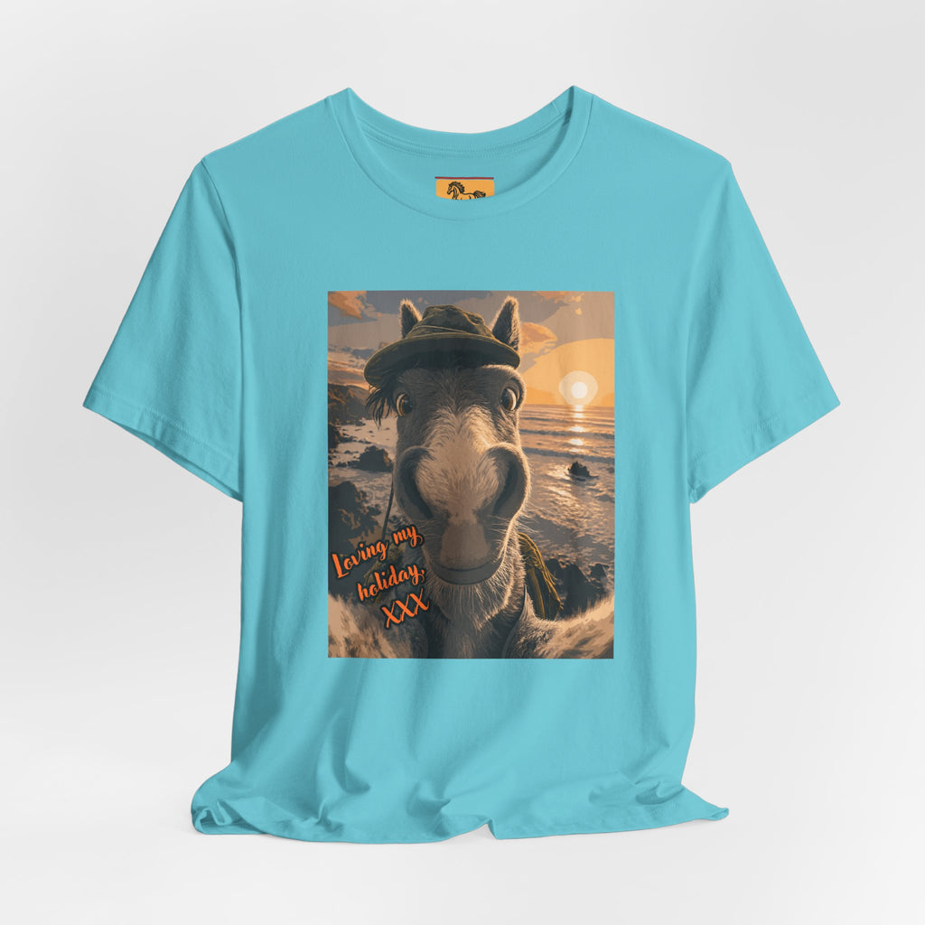 A Bella + Canvas 3001 unisex t-shirt featuring an illustrated horse taking a beach selfie at sunset, wearing a hat, with the words 'Loving my holiday XXX' in orange script. 