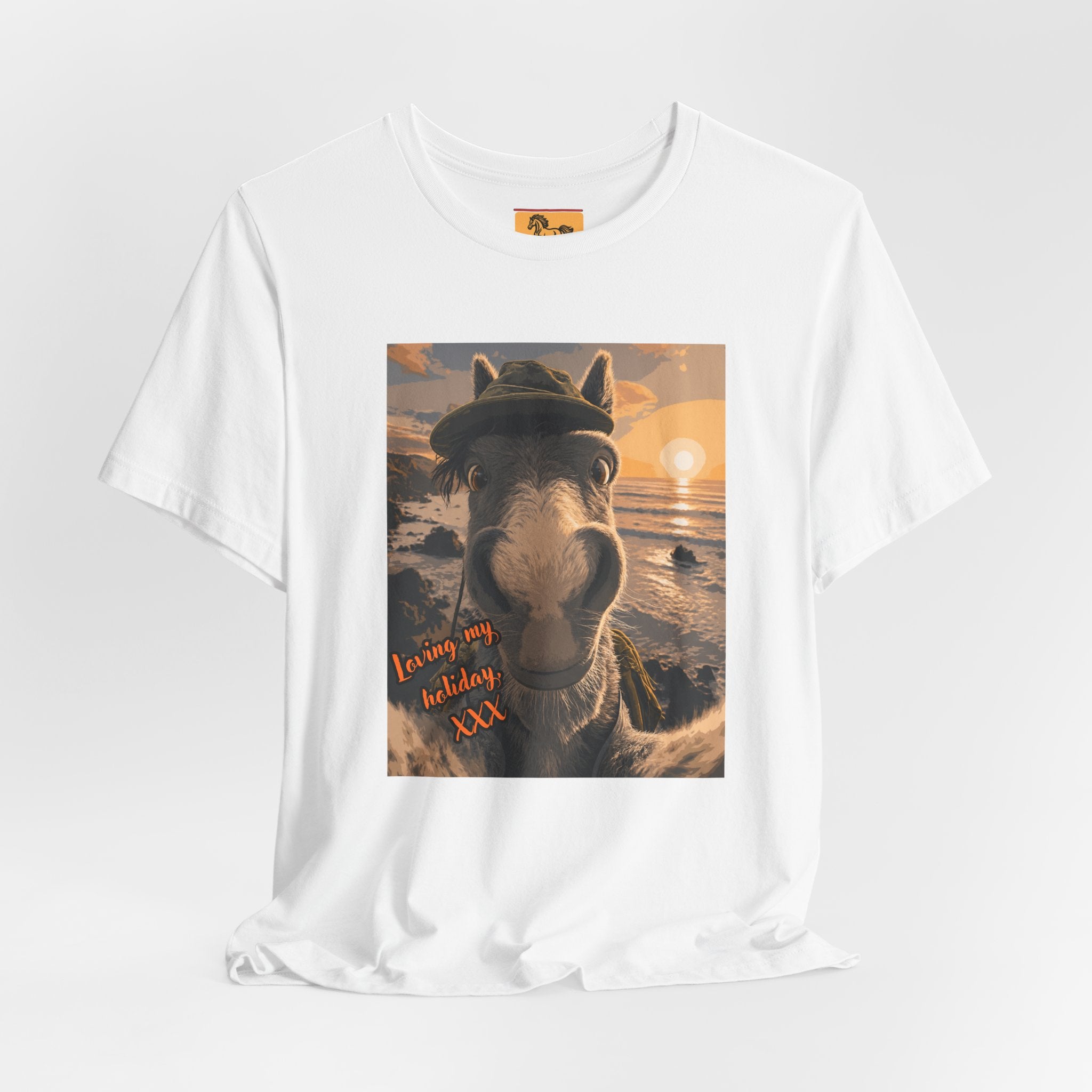 A Bella + Canvas 3001 unisex t-shirt featuring an illustrated horse taking a beach selfie at sunset, wearing a hat, with the words 'Loving my holiday XXX' in orange script. 