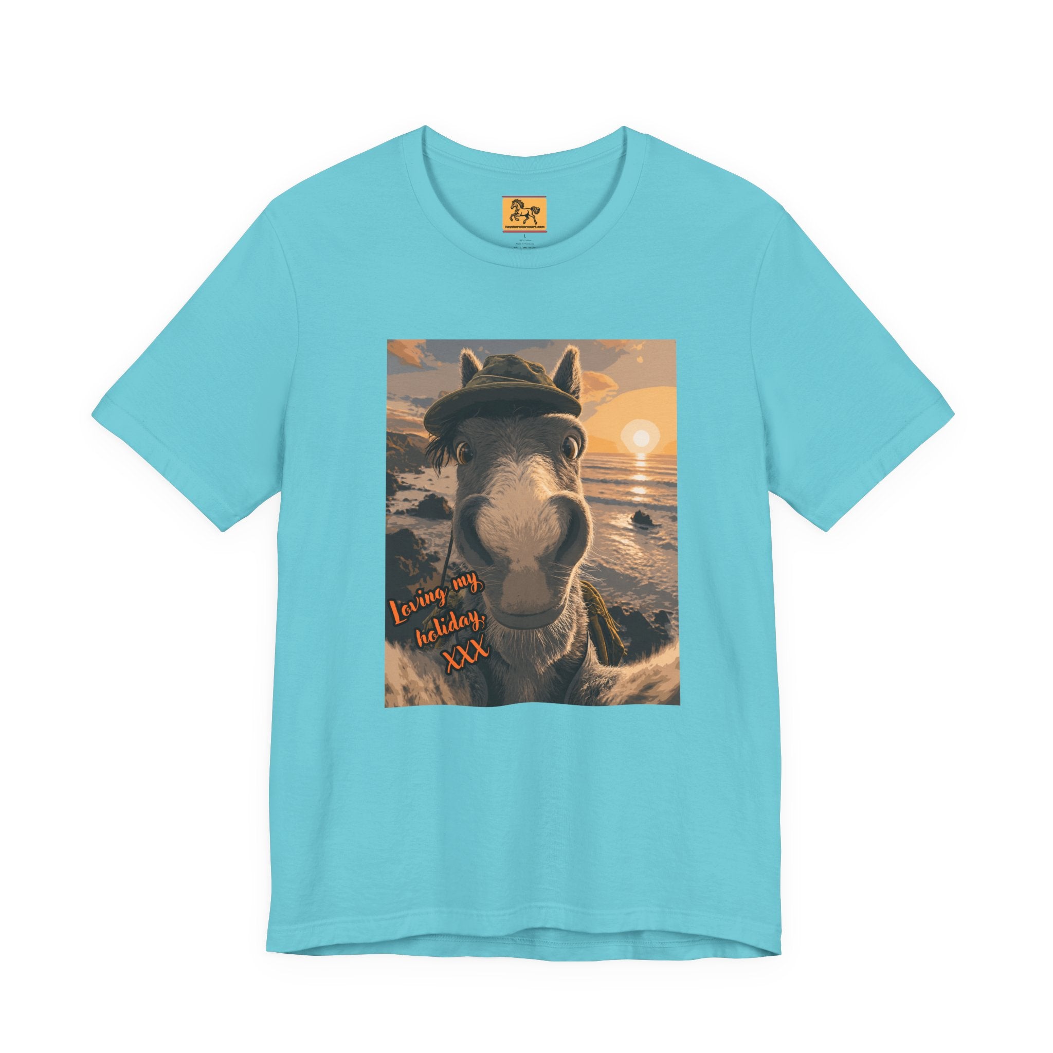 A light blue Bella + Canvas 3001 unisex t-shirt featuring an illustrated horse taking a beach selfie at sunset, wearing a hat, with the words 'Loving my holiday XXX' in orange script. 