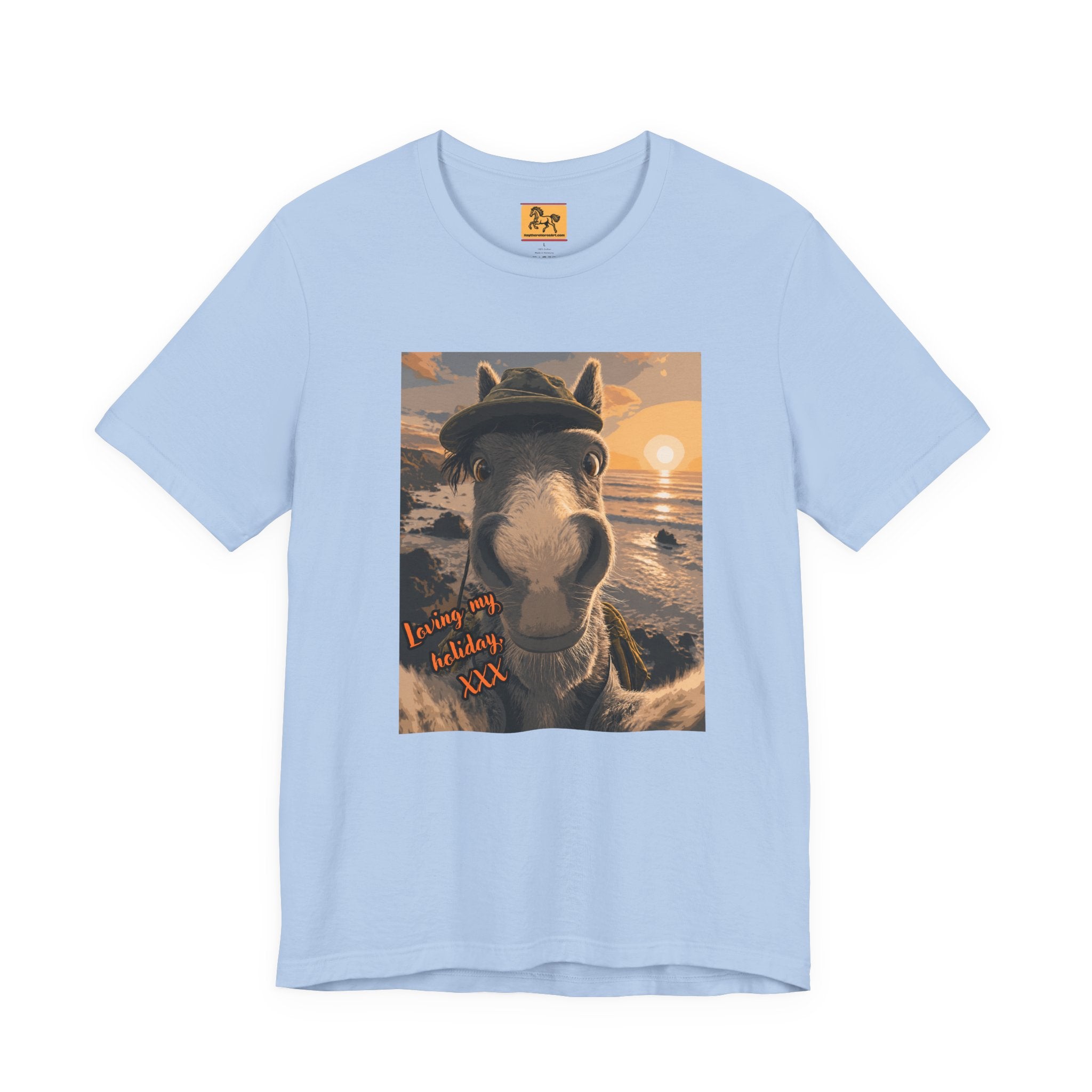 A light blue Bella + Canvas 3001 unisex t-shirt featuring an illustrated horse taking a beach selfie at sunset, wearing a hat, with the words 'Loving my holiday XXX' in orange script. 