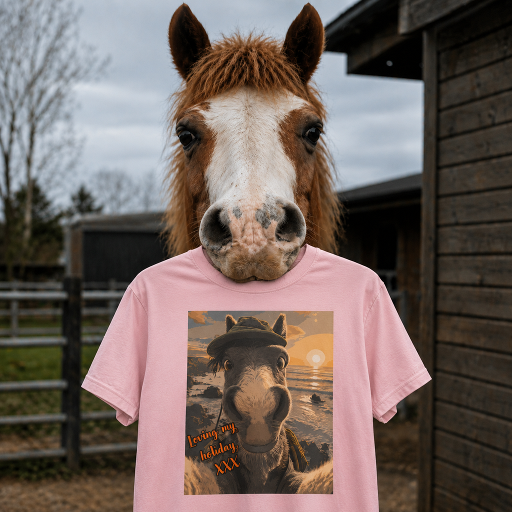 A chestnut pony holding a Bella + Canvas 3001 unisex t-shirt featuring an illustrated horse taking a beach selfie at sunset, wearing a hat, with the words 'Loving my holiday XXX' in orange script. 