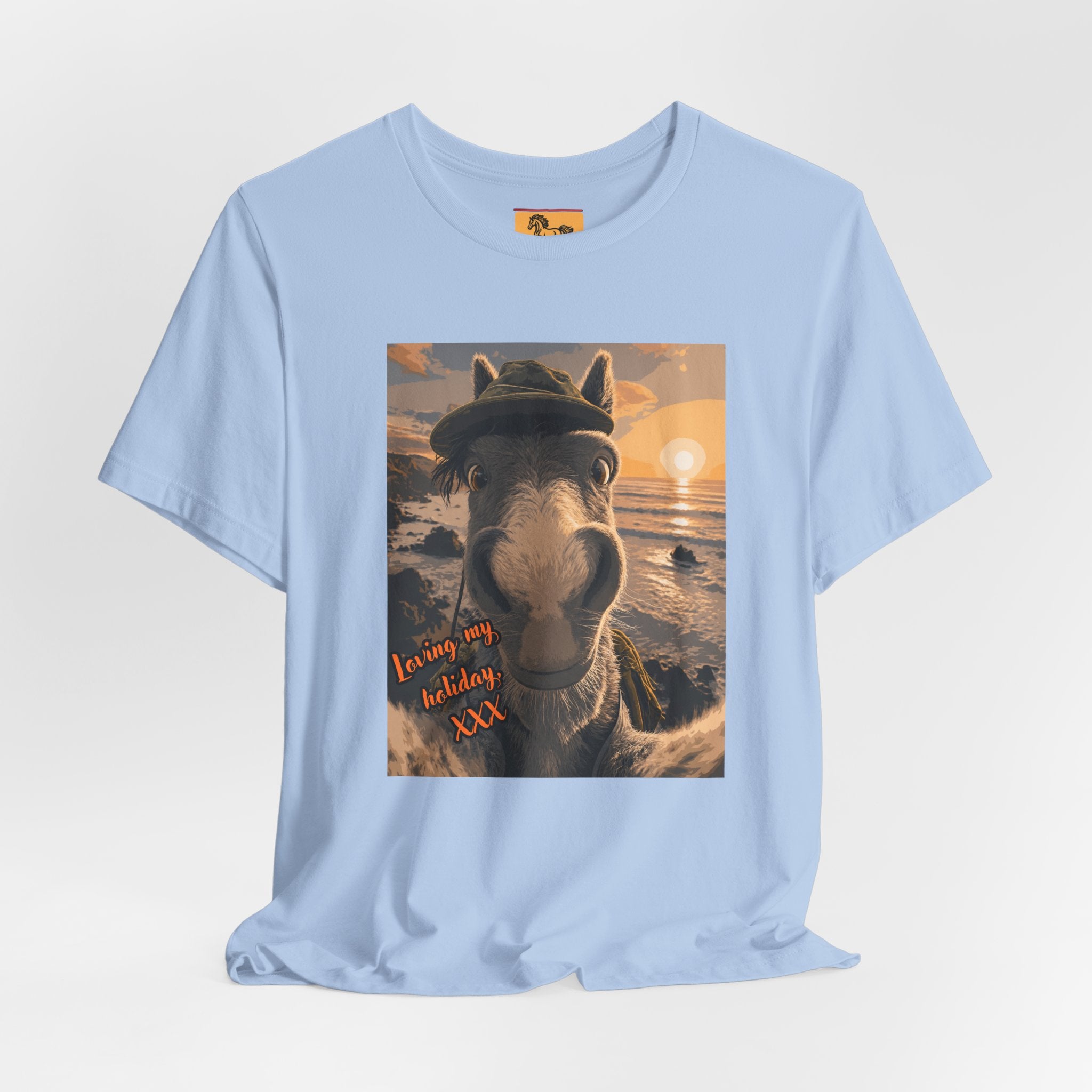 A Bella + Canvas 3001 unisex t-shirt featuring an illustrated horse taking a beach selfie at sunset, wearing a hat, with the words 'Loving my holiday XXX' in orange script. 