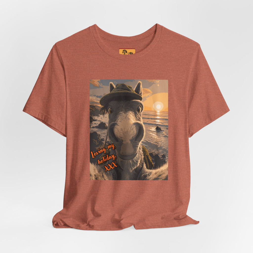 A Bella + Canvas 3001 unisex t-shirt featuring an illustrated horse taking a beach selfie at sunset, wearing a hat, with the words 'Loving my holiday XXX' in orange script. 