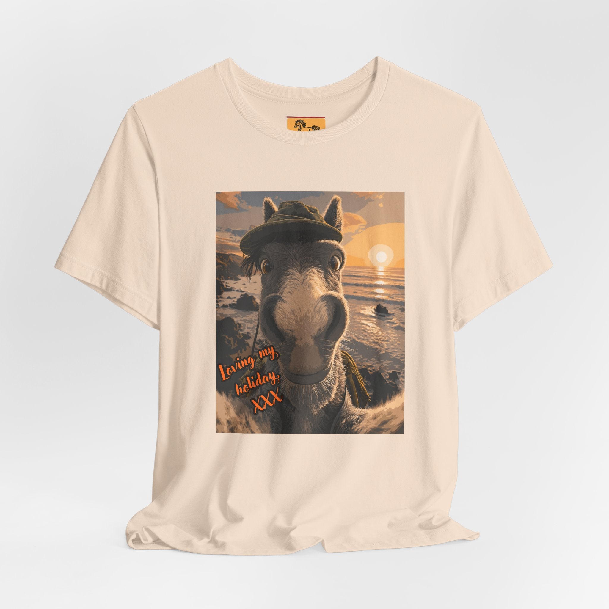 A Bella + Canvas 3001 unisex t-shirt featuring an illustrated horse taking a beach selfie at sunset, wearing a hat, with the words 'Loving my holiday XXX' in orange script. 