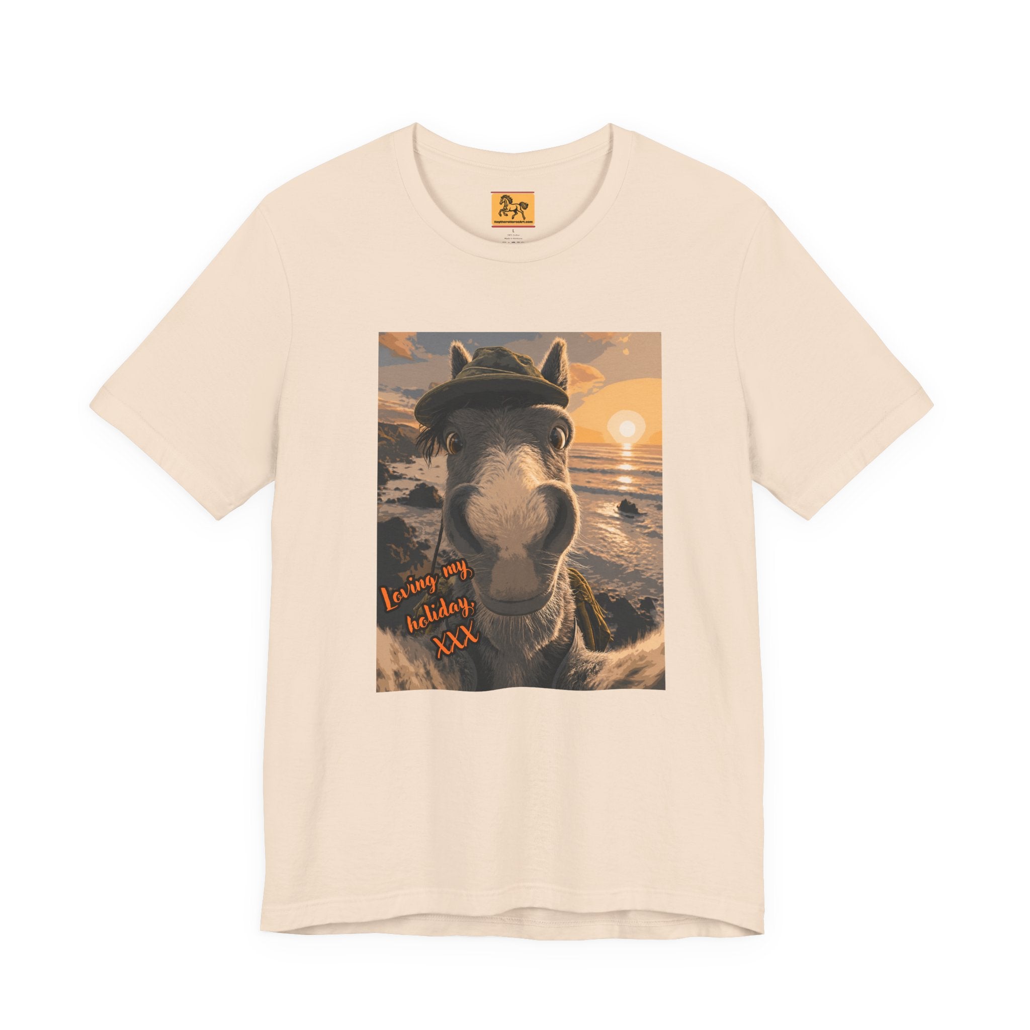 A cream Bella + Canvas 3001 unisex t-shirt featuring an illustrated horse taking a beach selfie at sunset, wearing a hat, with the words 'Loving my holiday XXX' in orange script. 